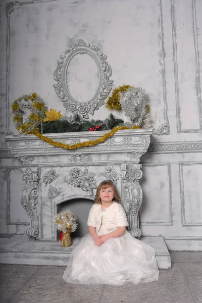 Niña en un vestido blanco y un abrigo de piel junto a la antigua chimenea en el — Foto de Stock