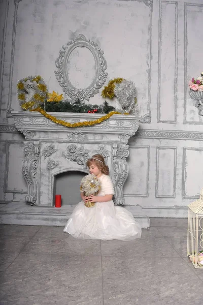 Niña en un vestido blanco y un abrigo de piel junto a la antigua chimenea en el — Foto de Stock