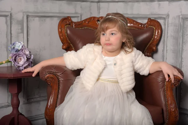 Girl in a white dress and a fur coat sits — Stock Photo, Image