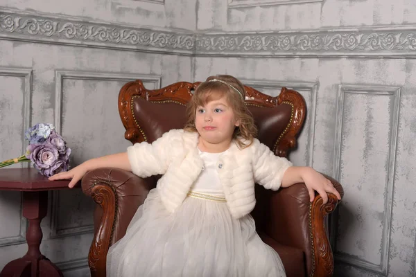 Menina em um vestido branco e um casaco de pele senta-se — Fotografia de Stock