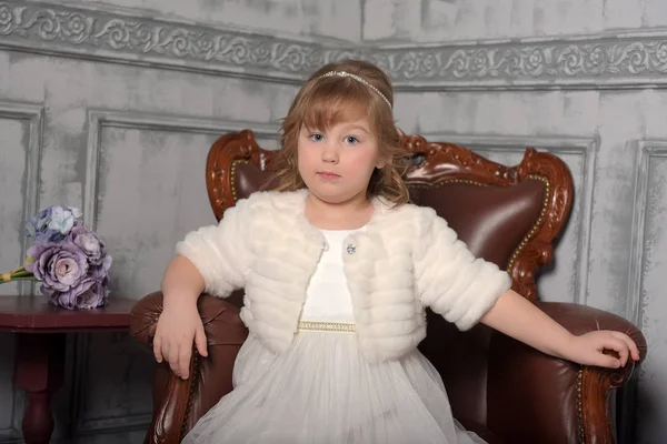 Girl in a white dress and a fur coat sits — Stock Photo, Image