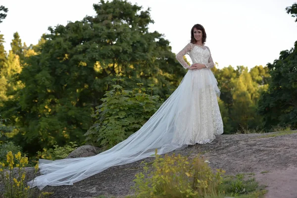 Woman in a white dress with a long train in the summer in a moun — Stok fotoğraf