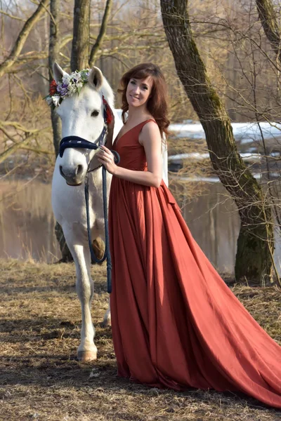 Kvinna i en röd lång klänning med en häst i naturen — Stockfoto