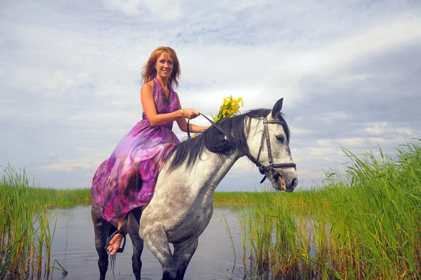 穿着紫色长裙的女人在水里骑马 — 图库照片