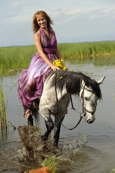 Žena ve fialových dlouhých šatech na koni ve vodě — Stock fotografie