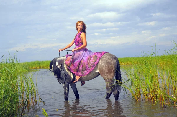 Žena ve fialových dlouhých šatech na koni ve vodě — Stock fotografie