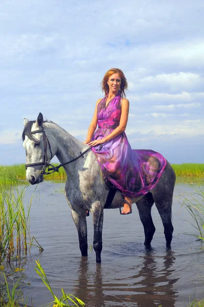 Mujer en un vestido largo púrpura montar a caballo en el agua en el —  Fotos de Stock