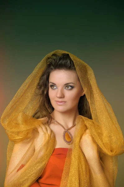 Portrait of a beautiful brunette woman in a golden cape — Stock Photo, Image