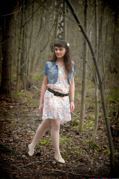 Una niña en un vestido ligero y chaqueta de mezclilla en el bosque entre los — Foto de Stock