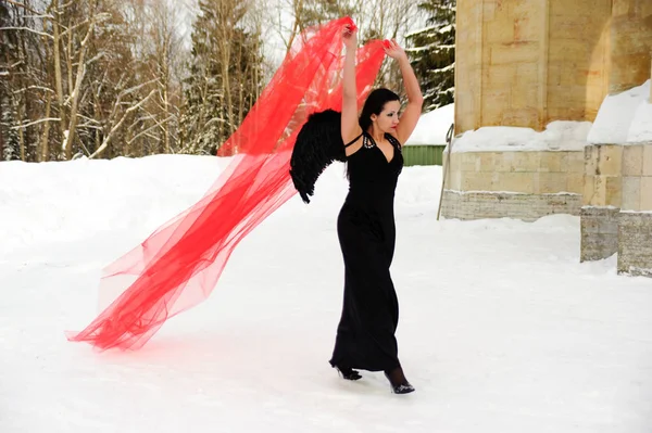 Meisje met zwarte engel vleugels in een zwarte jurk in de winter en rood f — Stockfoto