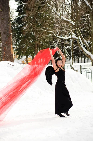 Meisje met zwarte engel vleugels in een zwarte jurk in de winter en rood f — Stockfoto