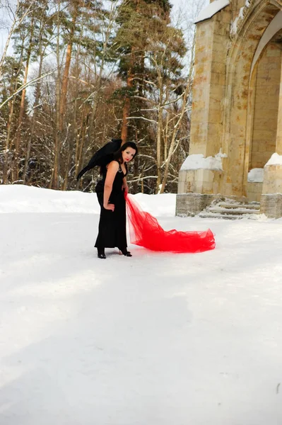 Girl with black angel wings in a black dress in winter and red f — Stock Photo, Image