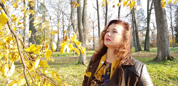 Mujer en una chaqueta de cuero en una rama de hojas de otoño en el pa —  Fotos de Stock