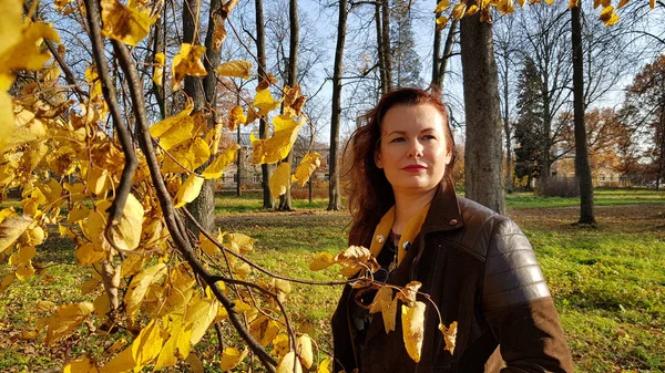 Mujer en una chaqueta de cuero en una rama de hojas de otoño en el pa — Foto de Stock