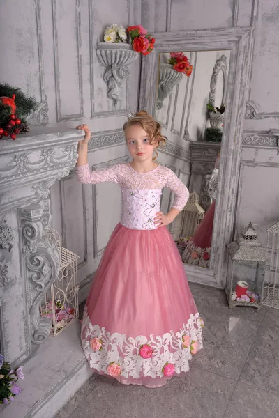 Jong meisje in een roze jurk bij de open haard — Stockfoto