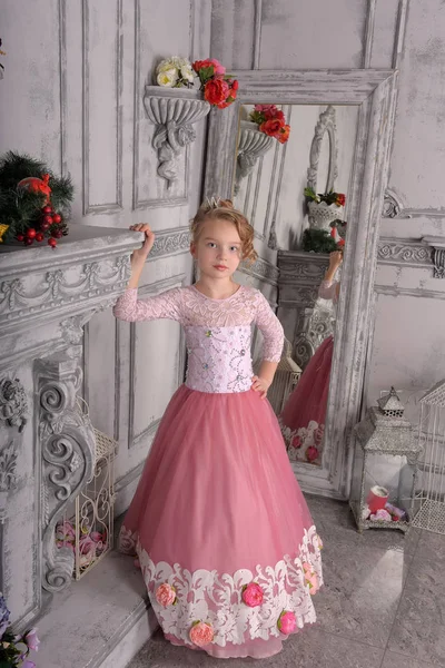 Niña en un vestido rosa junto a la chimenea — Foto de Stock