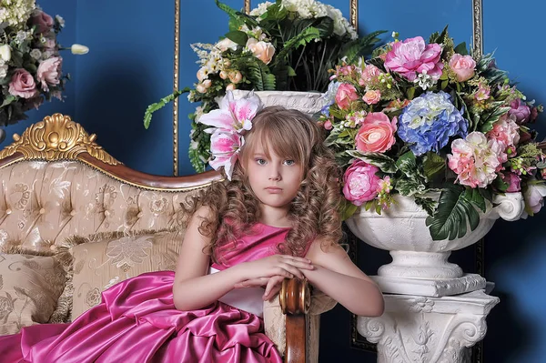 Klein meisje in een roze jurk onder de bloemen in de studio op t — Stockfoto