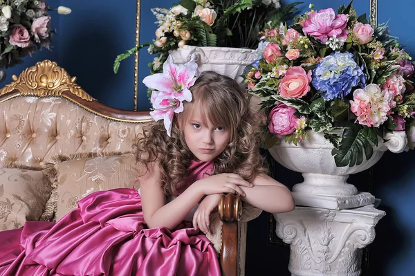 Little girl in a pink dress among the flowers in the studio on t — Stock Photo, Image