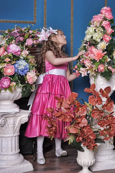 Klein meisje in een roze prinses jurk tussen de bloemen in de St — Stockfoto