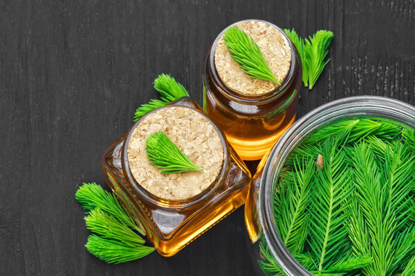 Homemade pine cough syrup for dry irritating throat coughs. Made from green young pine buds and honey.Alternative medicine concept on black wooden table, top view (selective focus).