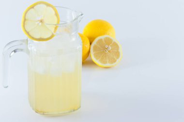 Limon dilimleriyle süslenmiş buzlu limon suyu beyaz bir arka planda ikiye bölünmüş.