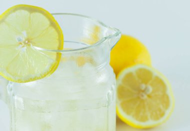 Limon dilimleriyle süslenmiş buzlu limon suyu beyaz bir arka planda ikiye bölünmüş.