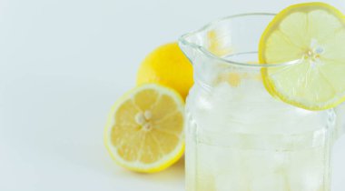 Limon dilimleriyle süslenmiş buzlu limon suyu beyaz bir arka planda ikiye bölünmüş.