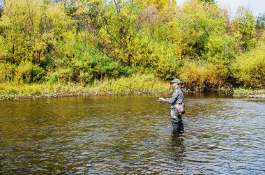 Küçük bir nehir üzerinde sonbahar Balık tutma. Balıkçı iplik ile nehrin ortasında duruyor. Rusya. Ural. Sulyom Nehri