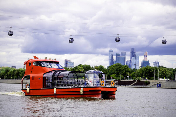 Scenic view of red cruise boat , tourist ship floating on the Moscow river ,  Moscow International Business Center and  cable car on the Sparrow hills
