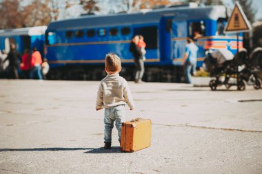 Yalnız trendy iki yıl yaşlı çocuk çocuk kahverengi retro çanta Tren İstasyonu trenin yanında poz. Arkadan görünüm.