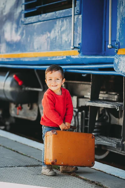 可爱的小孩男孩穿着红色毛衣在火车站附近火车与复古老棕色手提箱 准备休假 平台上的年轻旅客 — 图库照片