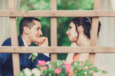 Gelin ve damat düğün buketiyle yaz terasında bir kafede oturuyor.