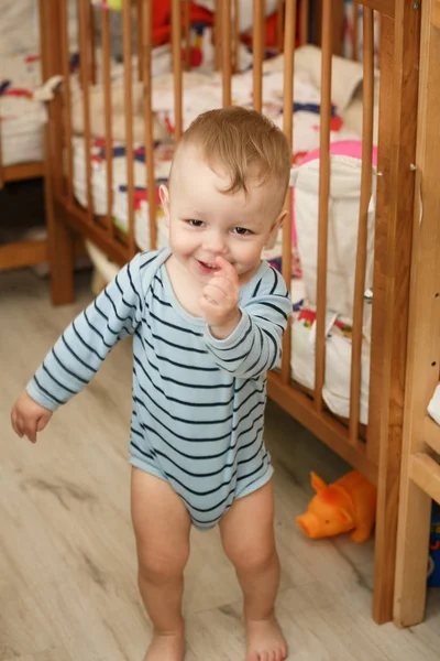 The baby is standing in a room near her baby crib. The baby hold — Stock Photo, Image