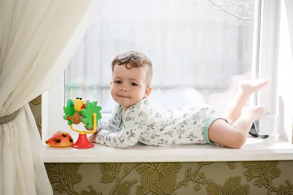 Mignon petit garçon bouclé est couché sur le rebord de la fenêtre — Photo