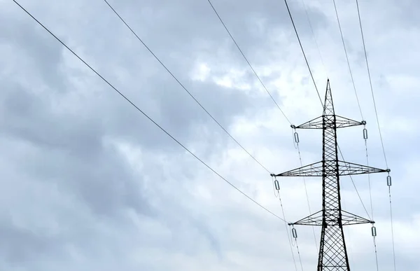 Power line in front of cloudy skies as silhouette
