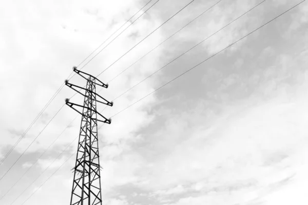 Power line in front of cloudy skies as silhouette in black and white