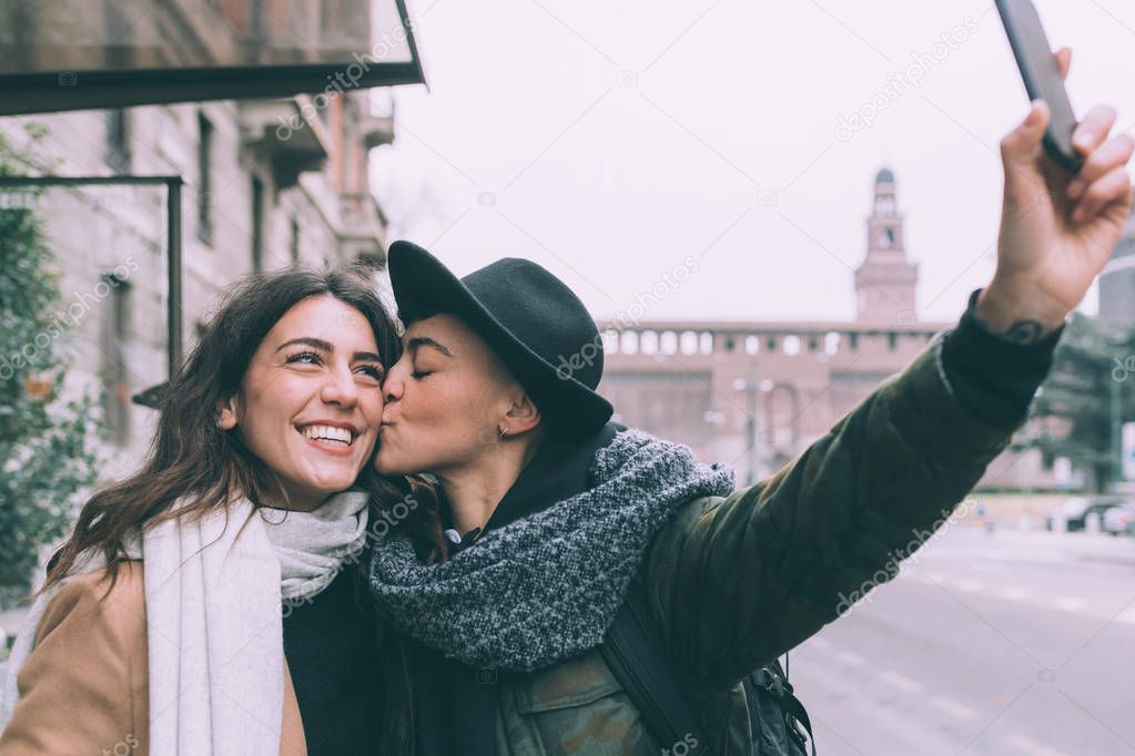 two women lesbian couple outdoors using smart phone taking selfie - technology, social network, sharing concept