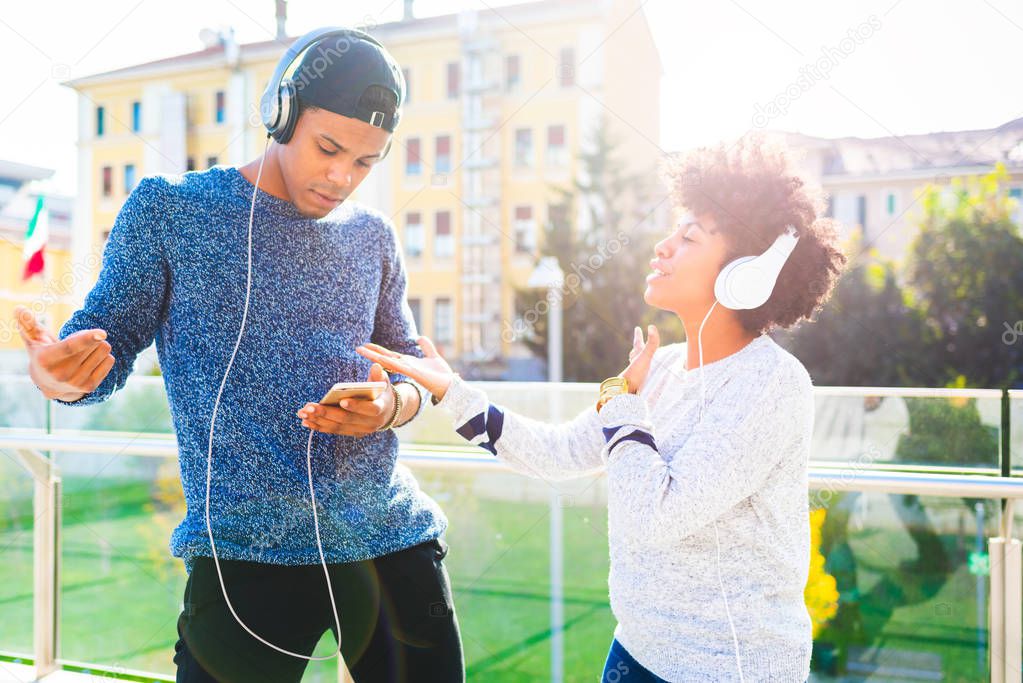 young couple multiracial listening music dancing outdoor back light using headphones and smartphone