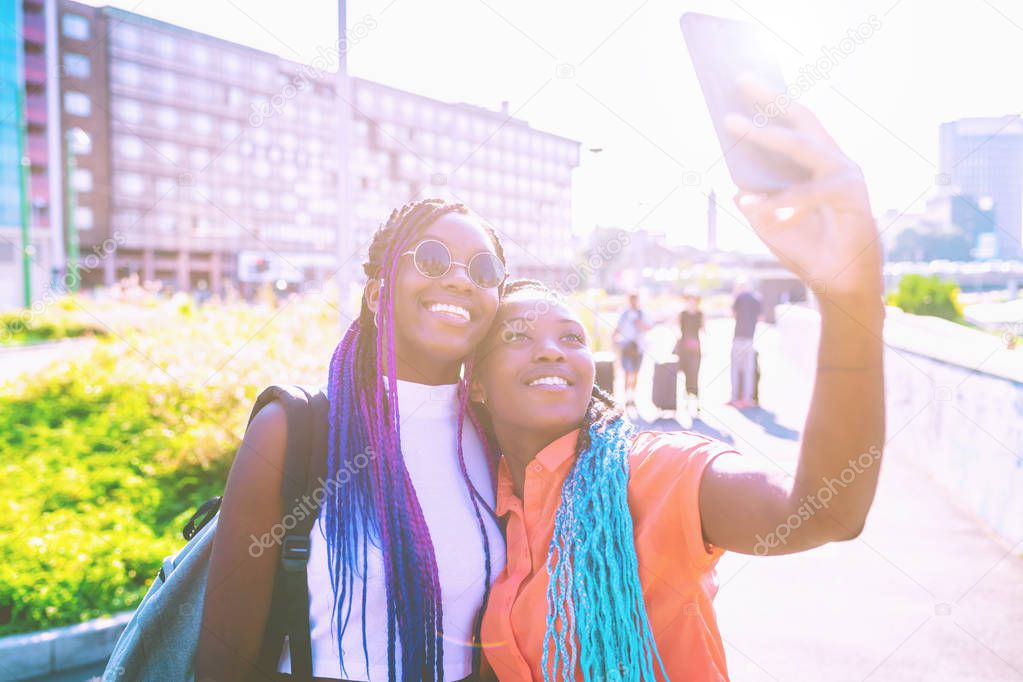 two sisters black siblings outdoor city back light using smart phone taking selfie smiling - happiness, social network, interaction concept