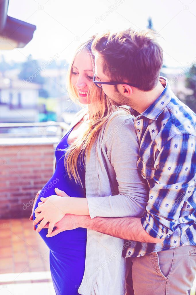 young pregnant couple indoors bedroom kissing - in love, new life, life event concept