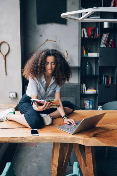 Jong krullend vrouw zitten op tafel met laptop — Stockfoto