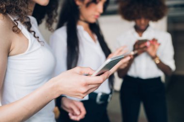 Ayakta duran ve akıllı telefonla veri paylaşan üç genç iş kadını