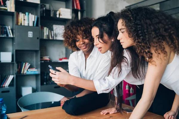 Tre unge multietniske venner som ser på smarttelefonen i moderne coworking – stockfoto