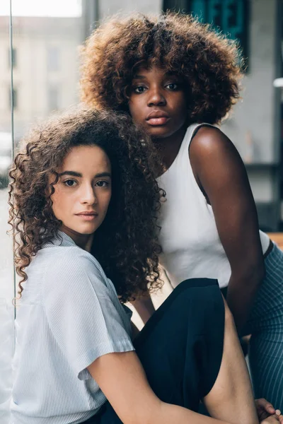 Dos jóvenes mujeres multiétnicas y rizadas posando juntos mirando cámara — Foto de Stock