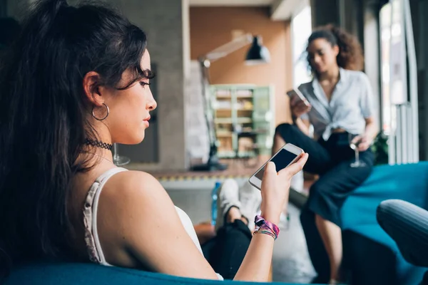 Dua wanita muda duduk di pub modern dan menggunakan smartphone — Stok Foto