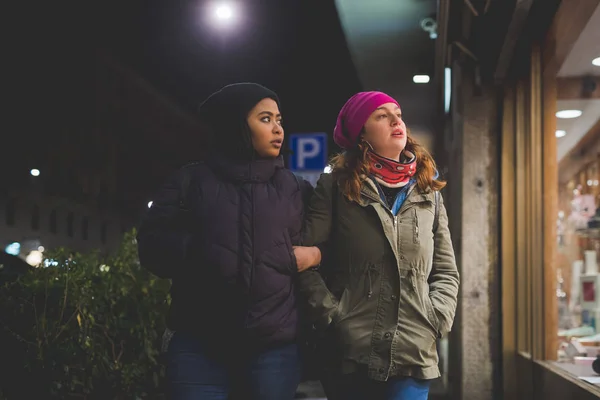 Две многорасовые женщины идут по улице и смотрят витрины магазинов — стоковое фото