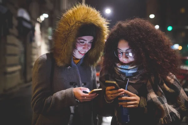 Dua wanita muda berdiri di jalan dan berinteraksi dengan smartphone — Stok Foto