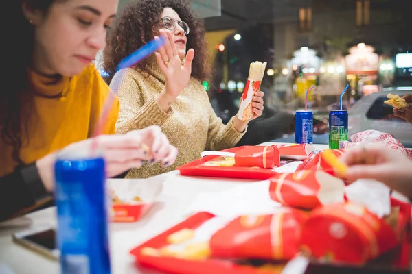 Genç kıvırcık kadın arkadaşlarıyla fast food yiyor. — Stok fotoğraf