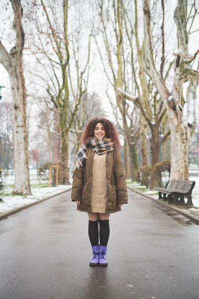 Portrait of young curly woman standing in tree lined avenue and smiling — Stock Photo, Image