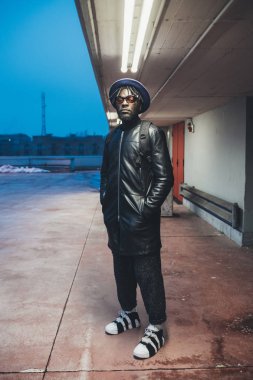 Genç siyahi adam sokakta dikiliyor ve kameraya bakıyor. 